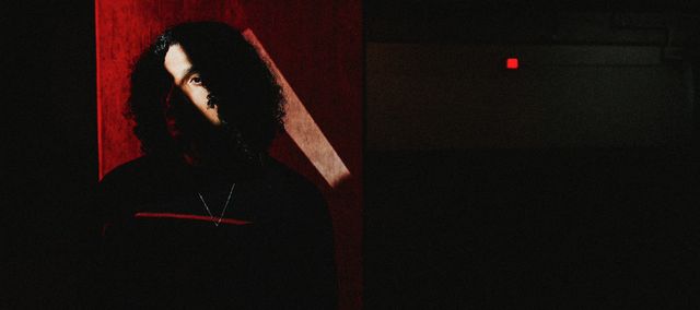 Eric Solitude basked in shadow, you can only see his outline on a red background.