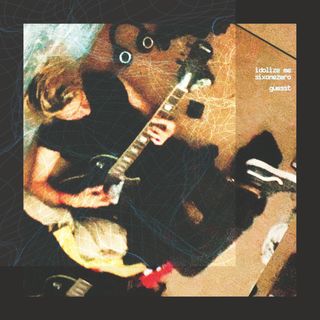 top down shot of guesst sitting down on the floor leaning against a mattress propped up against the wall. they're holding a guitar. there is headphones on the ground.