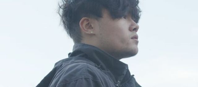 Seong in the day time with a background of a bright grey sky looking off to the left of the image wearing a grey coat.